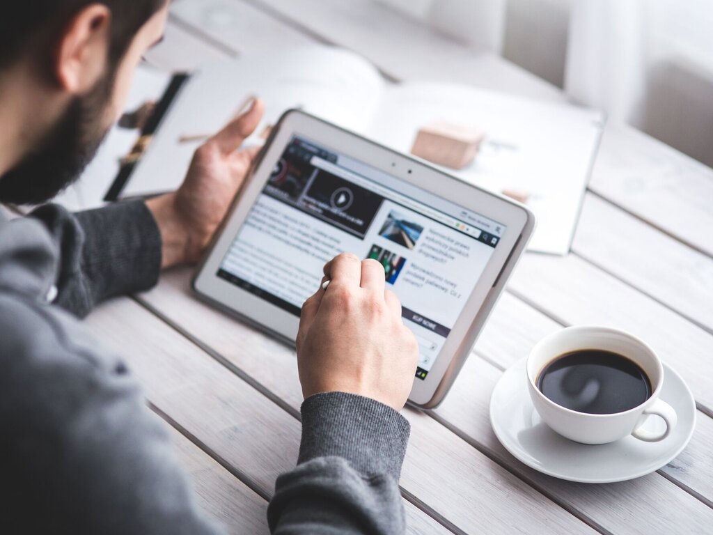 Man reading news on a tablet next to a coffee cup