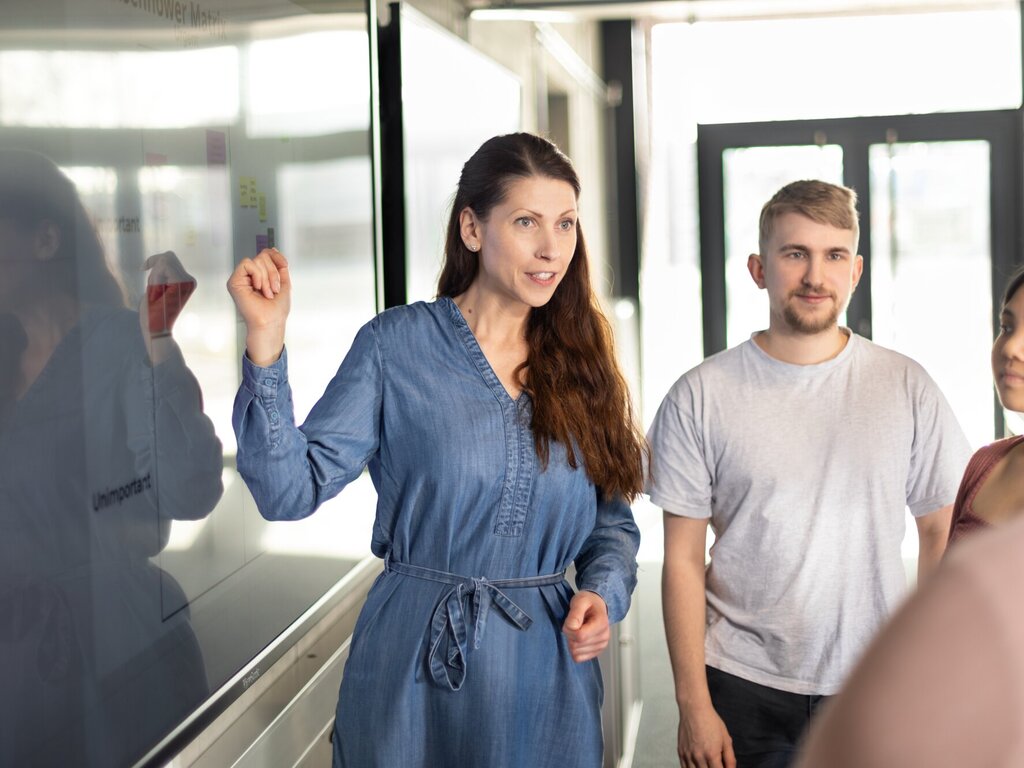 Lehrende erklärt Studierenden etwas an einem Wandbildschirm
