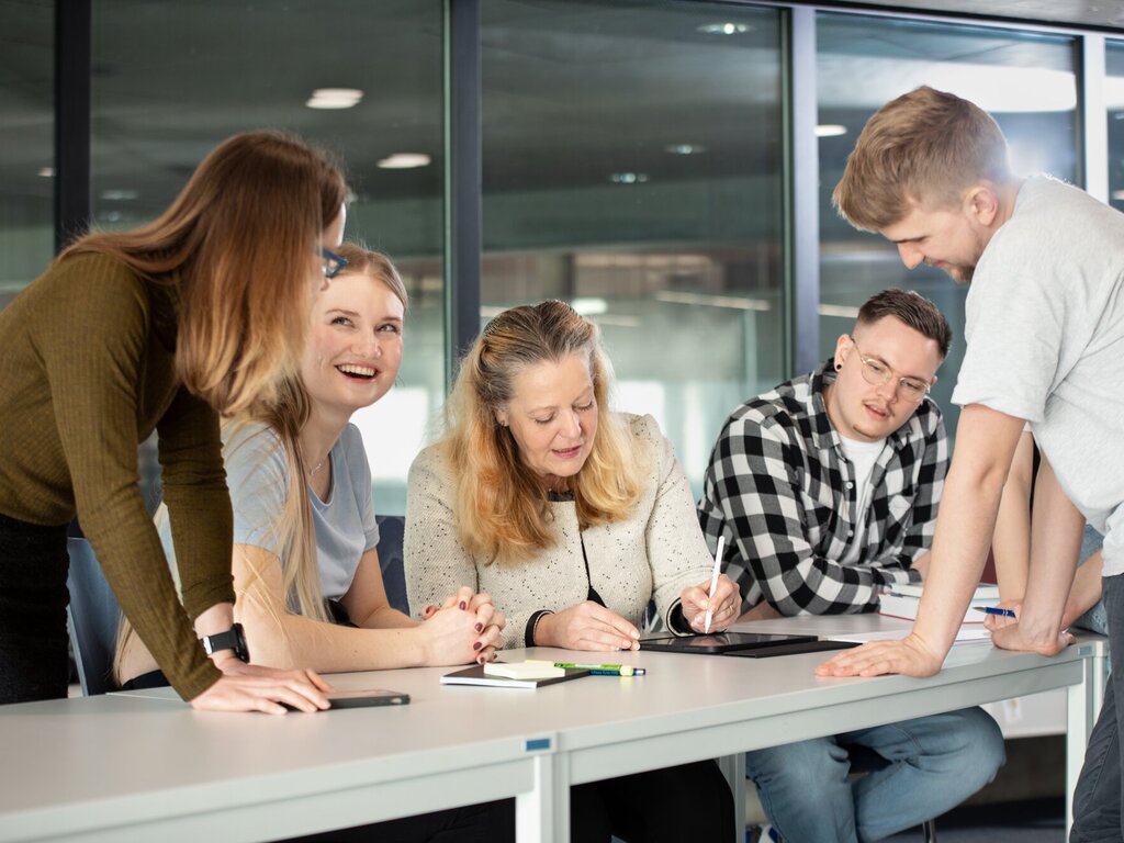 Professorin schreibt zwischen Studierenden sitzend auf einem Tablet
