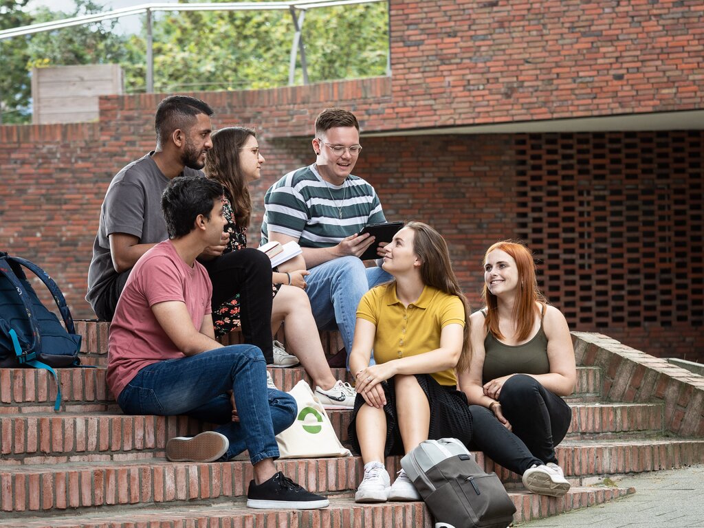 Eine Gruppe Studierender sitzt auf der Treppe vor Gebäude T