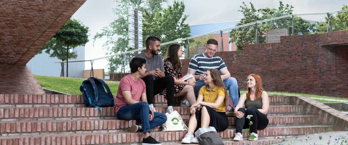Sechs Studierende sitzend vor dem Gebäude T